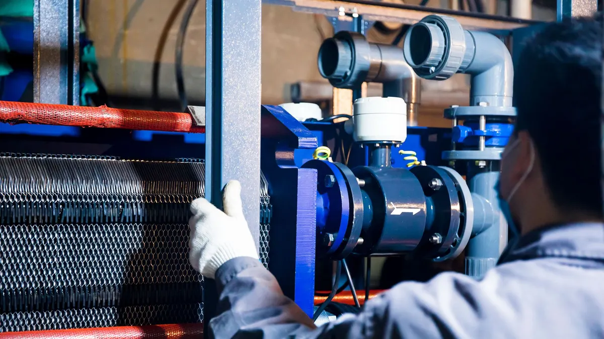 Technician checking a plate heat exchanger and pump skid in a plant room
